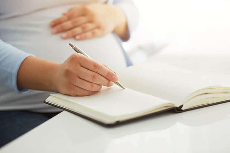 pregnant woman writing to her diary on table
