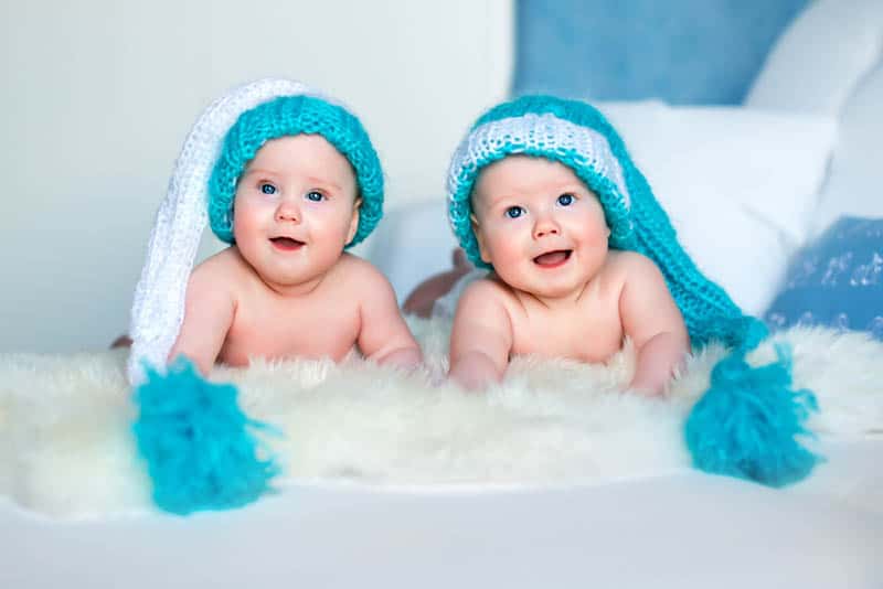 twin baby boys wearing funny hats on the bed
