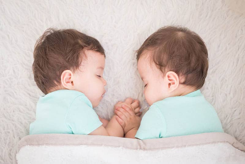 two cute twin babies sleeping together holding hands