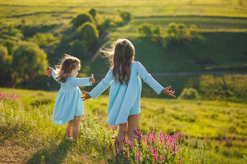 two little girls in dresses spreading arms in nature