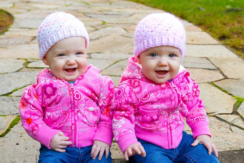two smiling twin girl babies sitting outdoor 