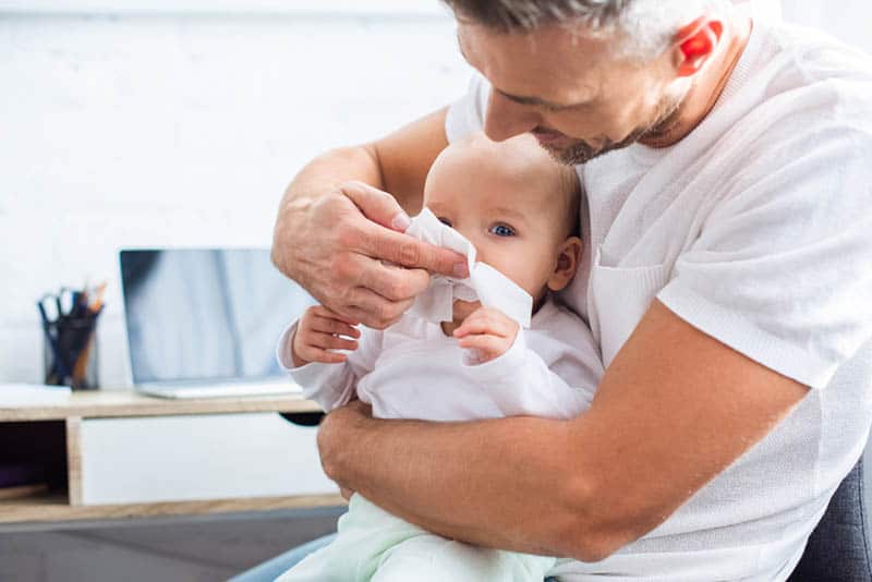 young father cleaning baby nose