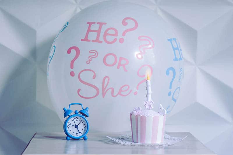A balloon he or she from a gender reveal party with sweet cake and alarm clock