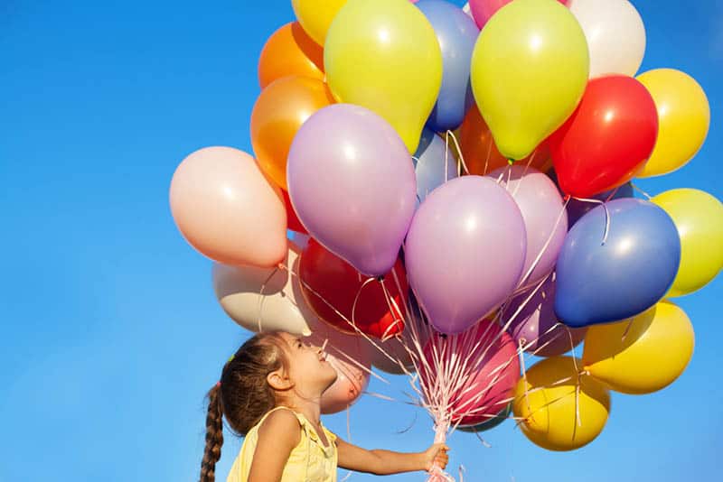 Happy little girl holding colorful balloons outdoors