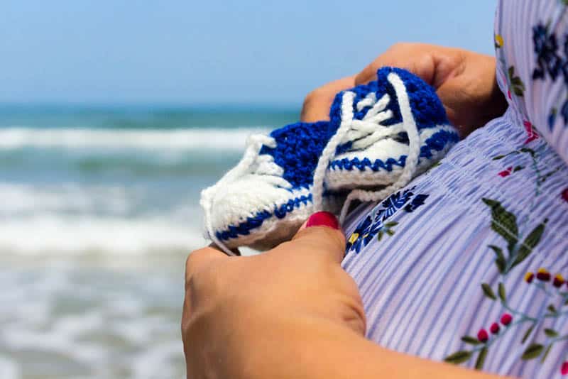 Pregnant Woman holding a pair of baby crochet sneakers on belly