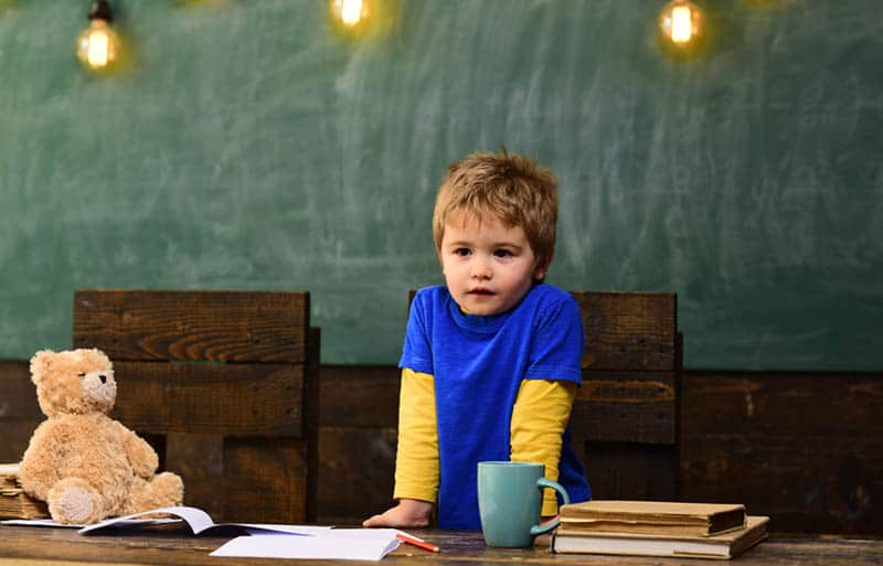 Small boy with serious face standing behind dark wooden table