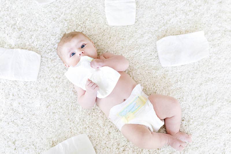 adorable baby boy lying on the floor with diapers all around