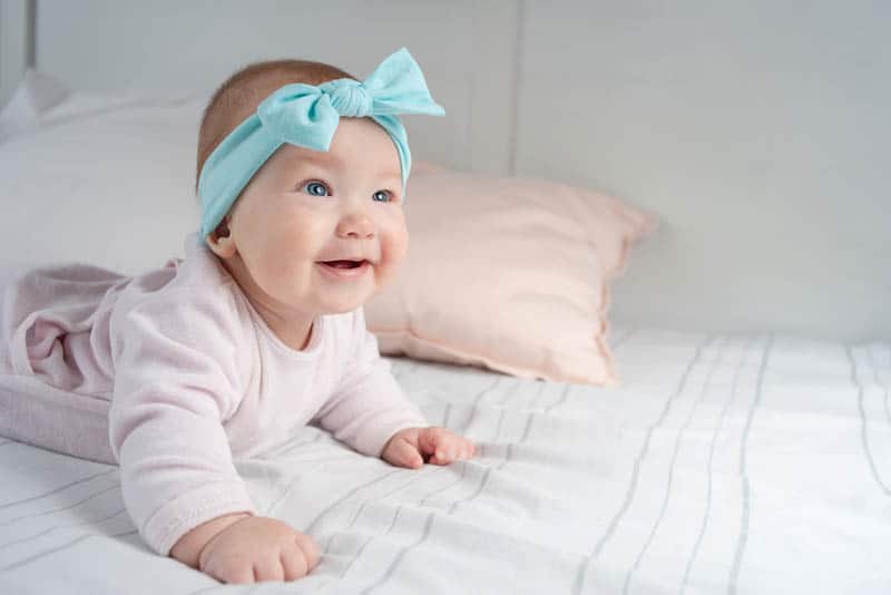 adorable baby girl wearing a blue headband and lying on the belly
