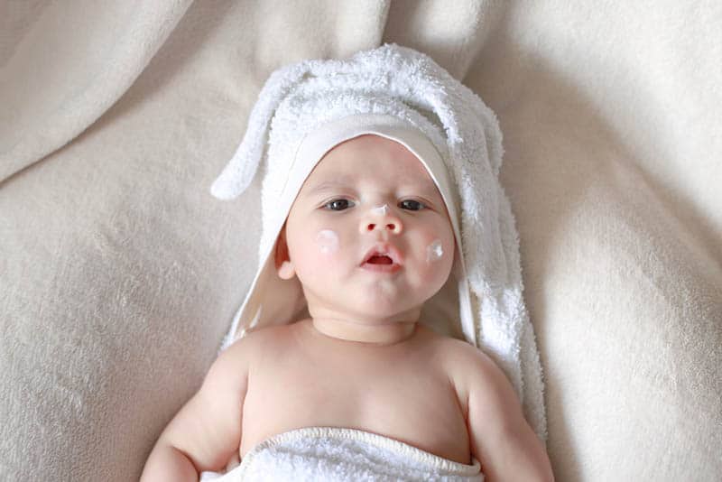 adorable baby lying in towel with cream on face