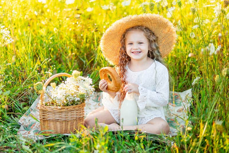 adorable little girl sitting in the field with flower basket