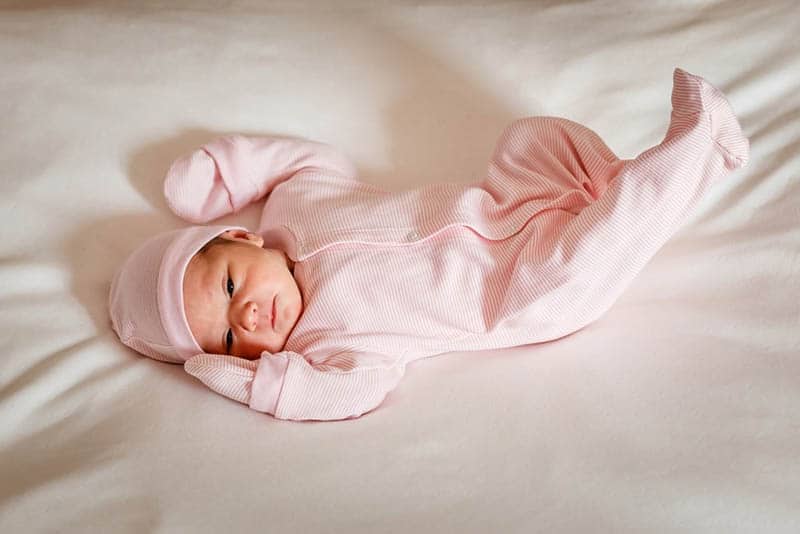 baby girl wearing onesie with hat and gloves lying on bed