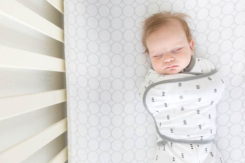 baby wearing cotton sack and sleeping in crib