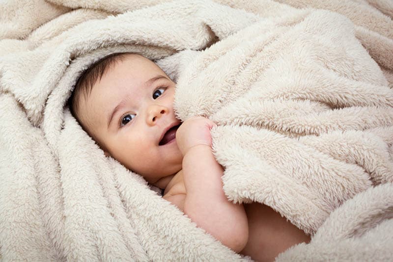 cute baby boy lying in bed under the fluffy blanket