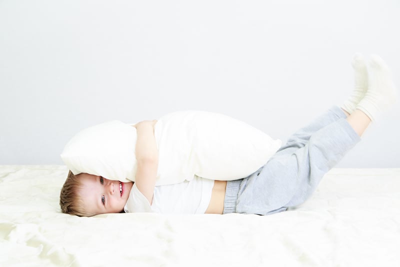 cute little boy hugging big white pillow on the bed