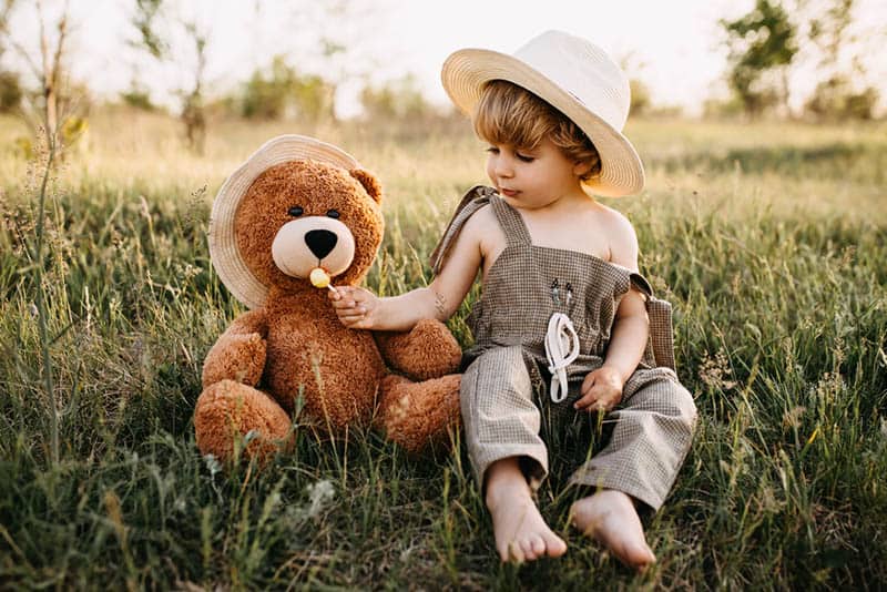 cute little boy sitting on grass with teddy bear