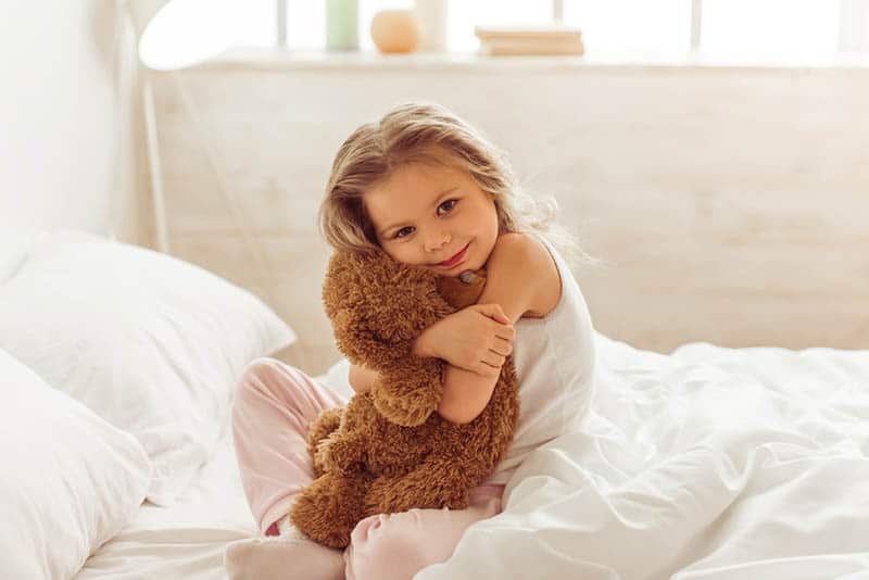 cute little girl hugging teddy bear on the bed