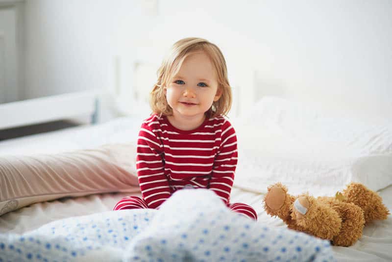 cute little girl in pajama sitting in her bed and smiling