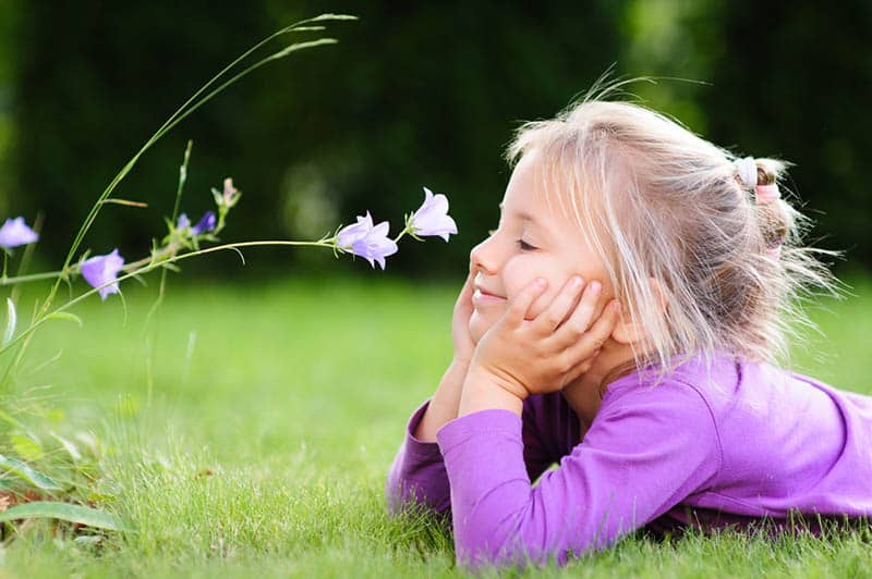 cute little girl lying in the garden and looking at a wild flower