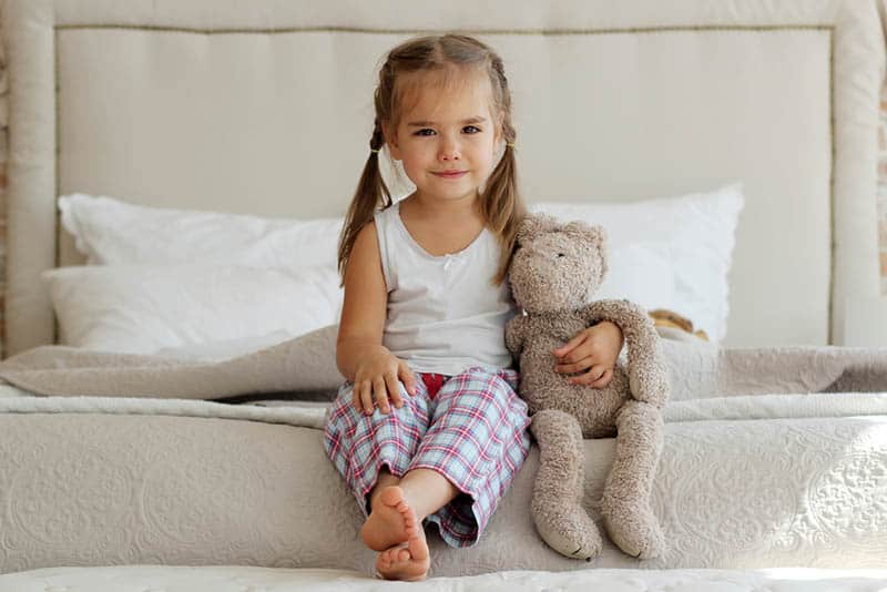 cute little girl sitting on the bed with her teddy bear toy
