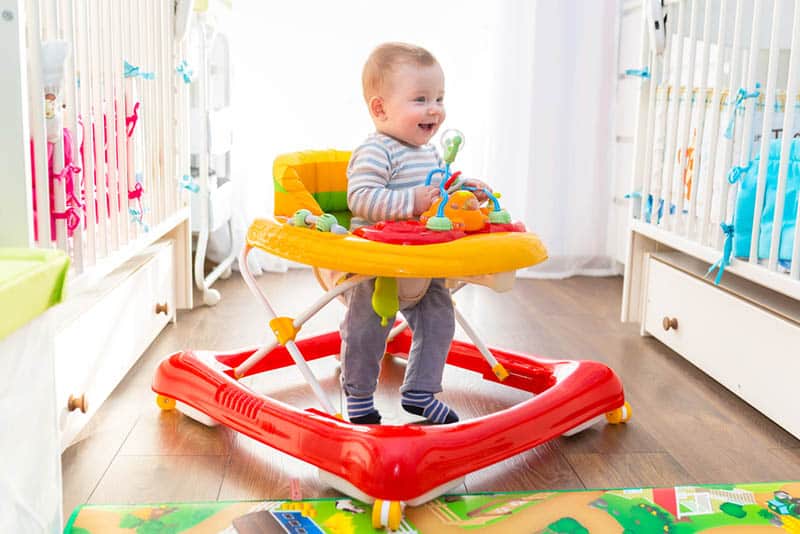 happy little baby walking at home in colorful walker