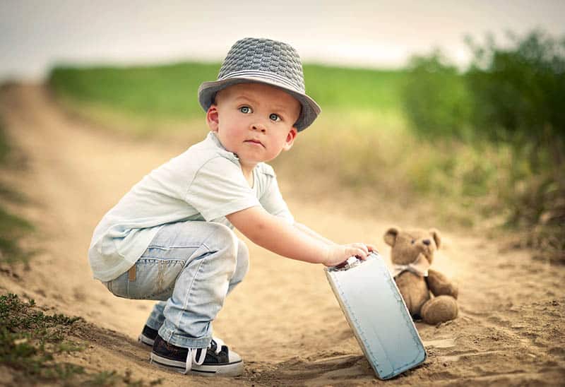 little boy holding a suitcase with teddy bear on the sand