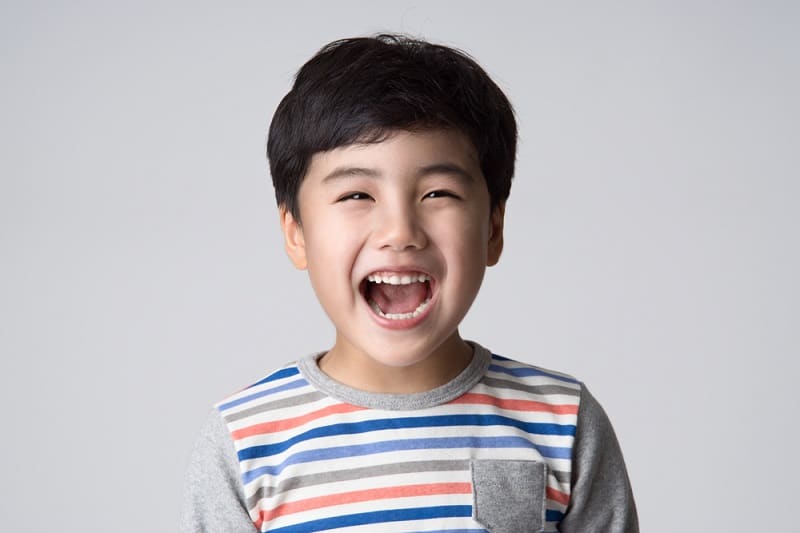 little boy with black hair wearing a striped shirt laughing