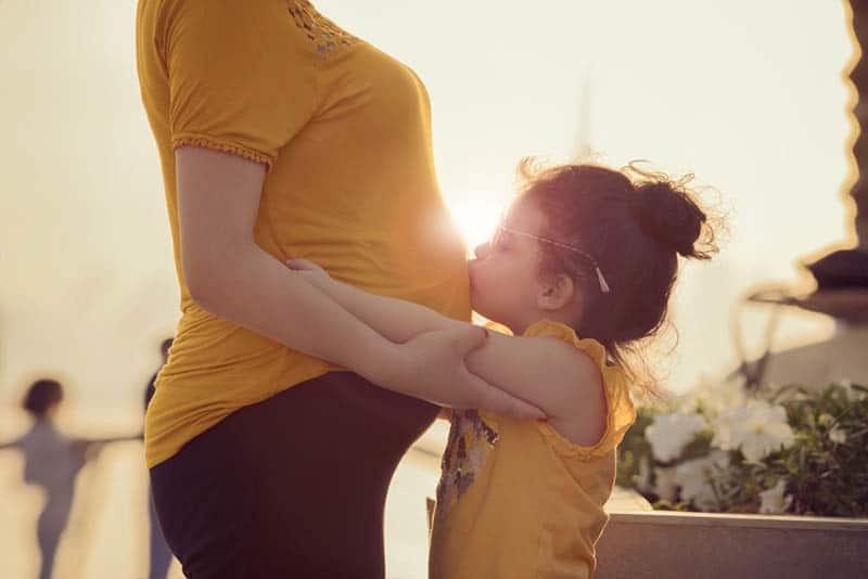 little girl kissing her pregnant mother's belly