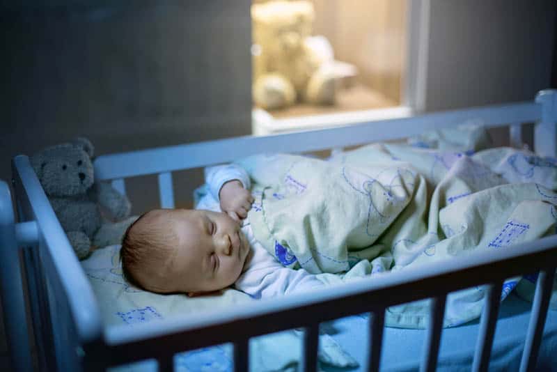 newborn baby sleeping in a crib covered with blanket at night