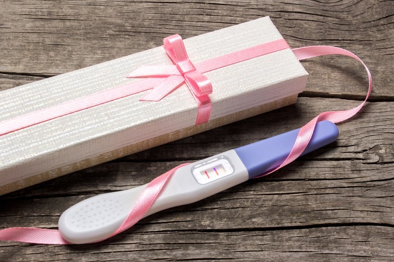 positive pregnancy test with a pink ribbon next to a gift box