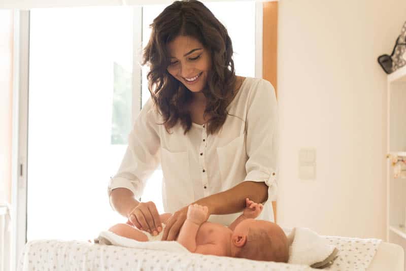 smiling mother changing diaper to her newborn baby in the bedroom