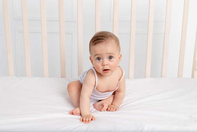 sweet baby boy sitting in crib on white mattress