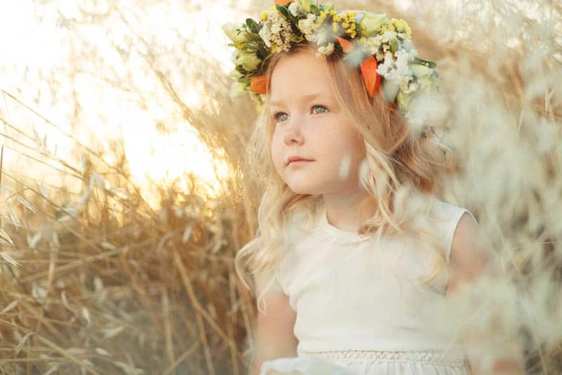 sweet little girl with flowers on her head sitting in meadow