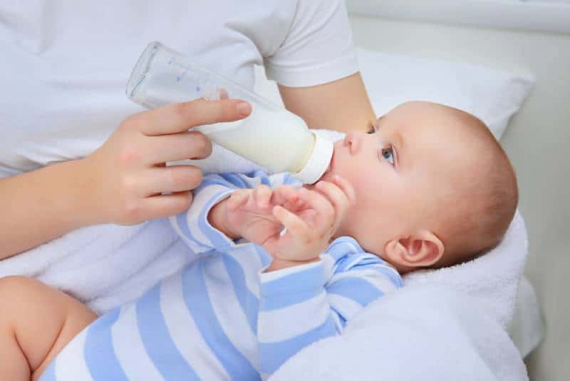 young mother holding baby in arms and feeding with milk bottle