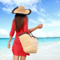 stylish woman walking by the ocean with a beach bag