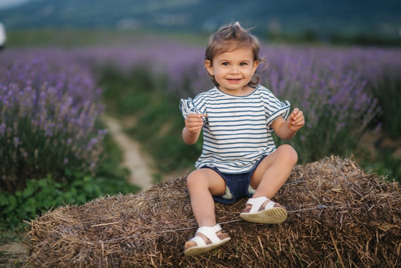 Adorable little girl sits on hay by the farm