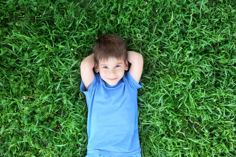 Cute little boy lying on green grass in park