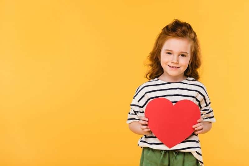 red-haired girl smiling and holding a red paper heart