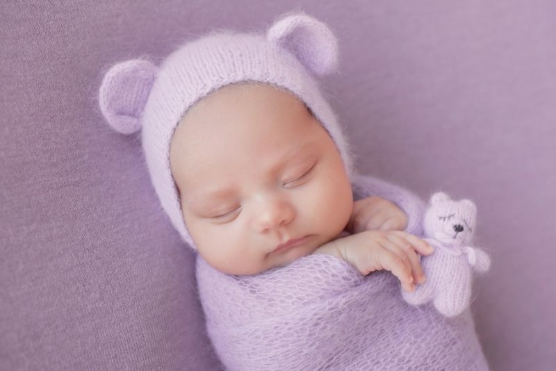 baby girl in a purple swaddle and funny hat with ears sleeping