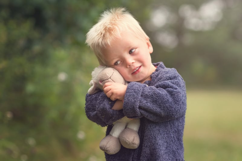 Little blond boy holding plush sheep in the park