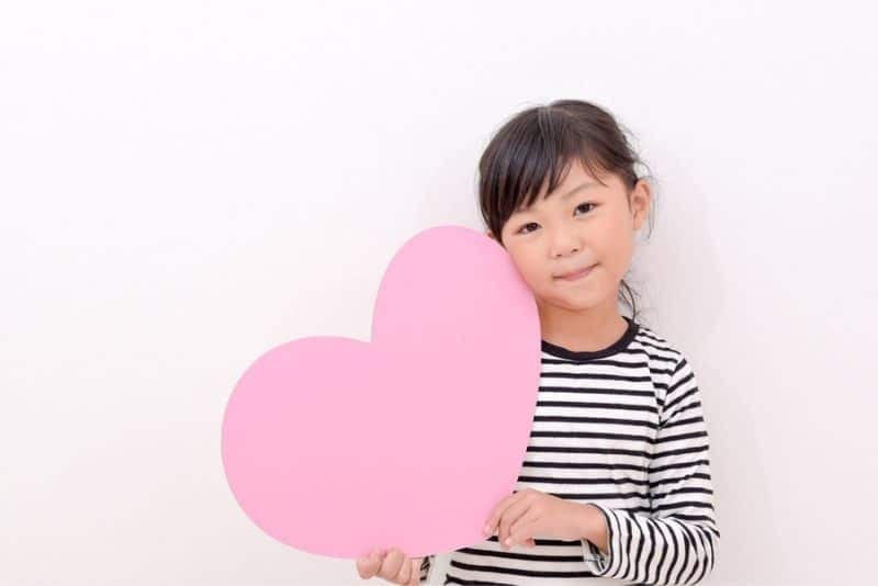 cute girl holding a pink paper heart and smiling