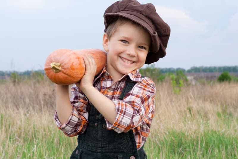 Smiling boy standing with pumpkin on his shoulder