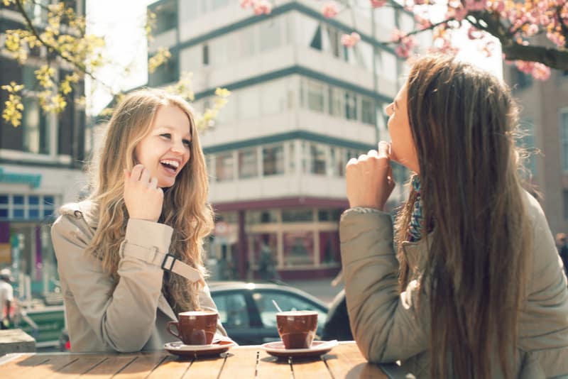 Two young women talk and drink coffee in cafe
