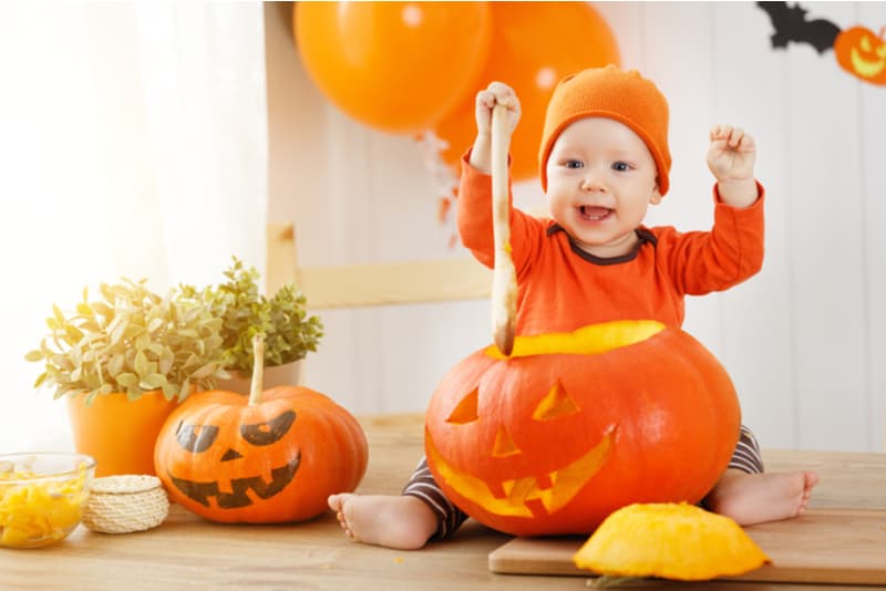 baby with a pumpkin for Halloween in the kitchen