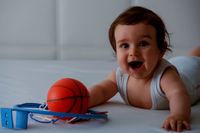happy baby boy playing with basketball on the bed