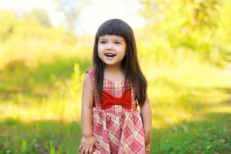 smiling little girl with long brown hair standing in a field