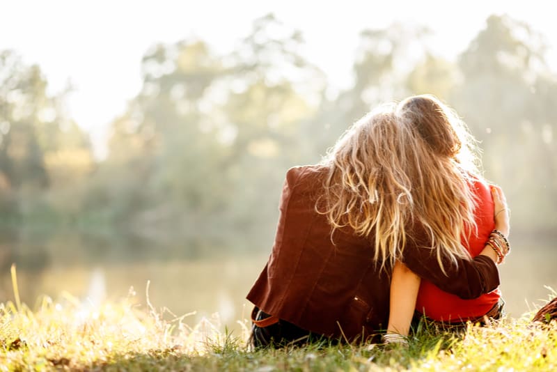 two young women sitting on grass hugging