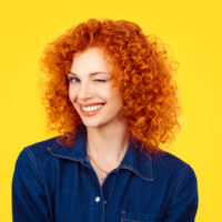 redhead woman with curly hair smiling and winking at the camera