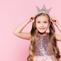 short little girl in a fancy dress puts a crown on her head