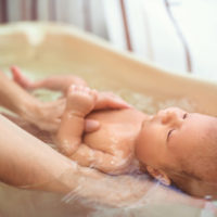 mother giving her baby a bath in a small plastic tub
