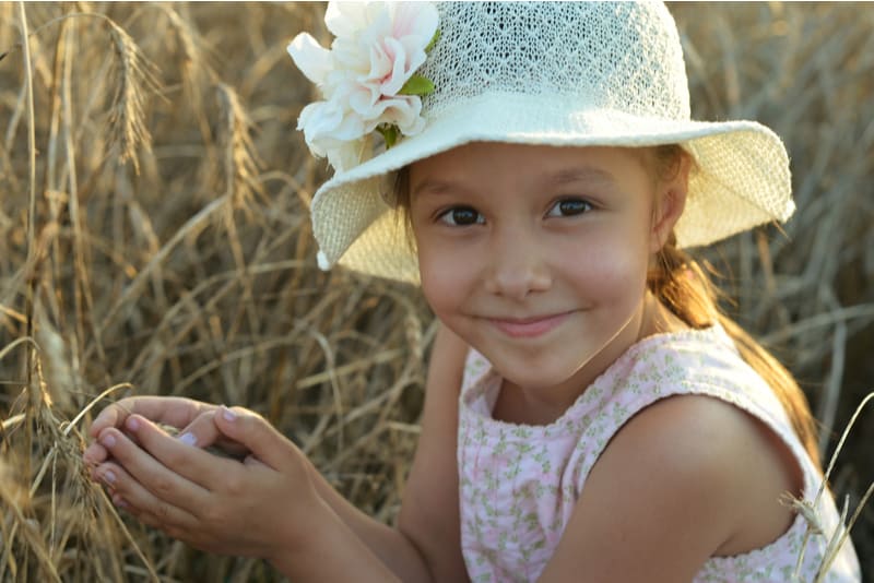 Cute little standing girl in the wheat field on sunset